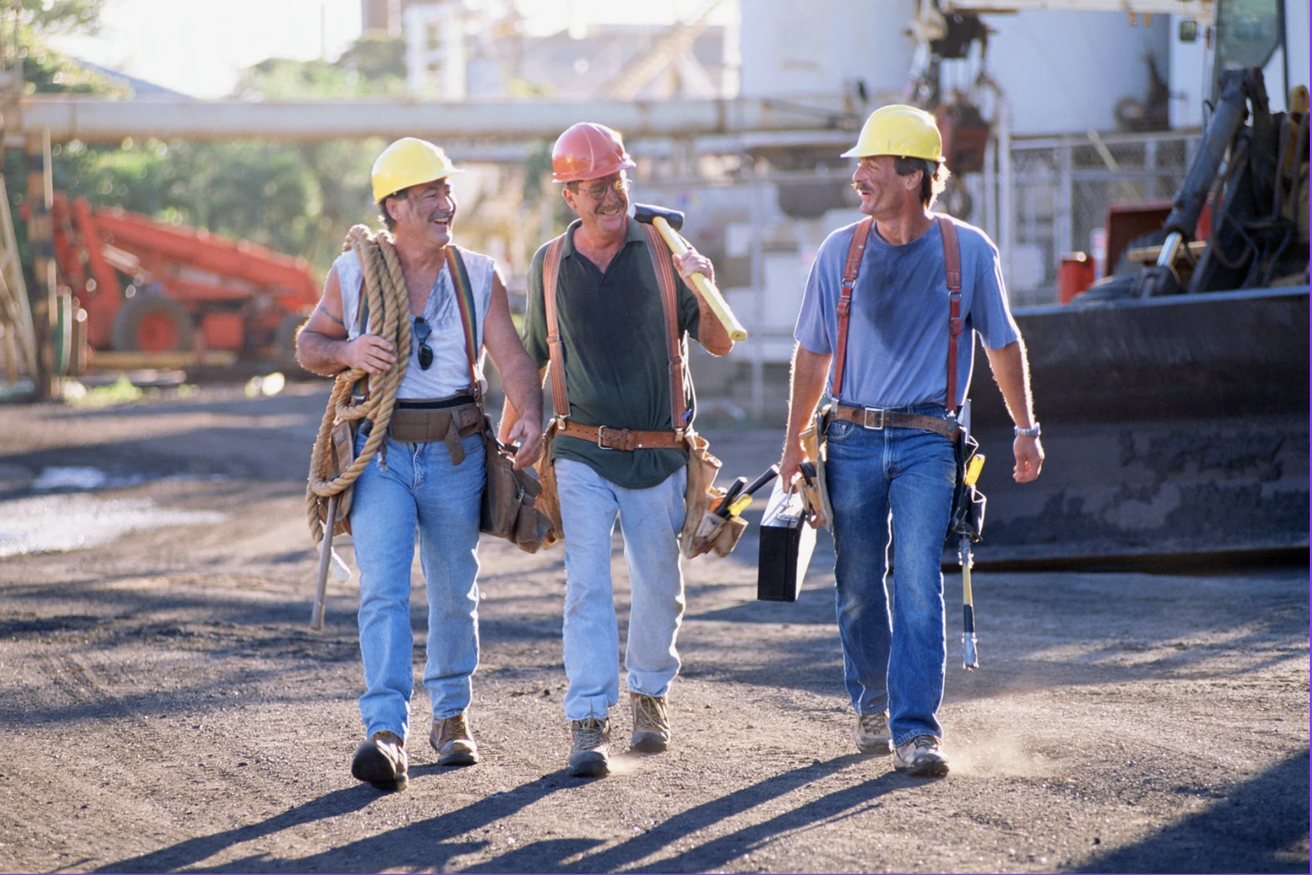 Three construction workers in hard hats and safety vests walking together on a job site